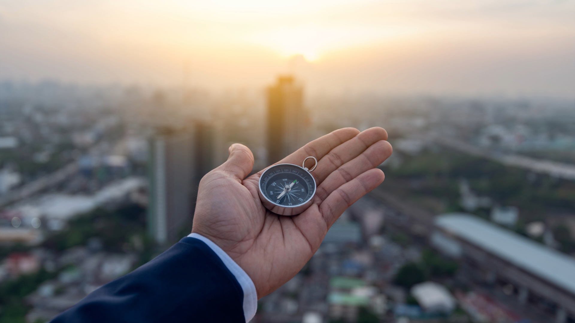 Businessman holding a compass in his open palm above a city skyline at sunrise, representing aviation marketing as a flight plan for business growth